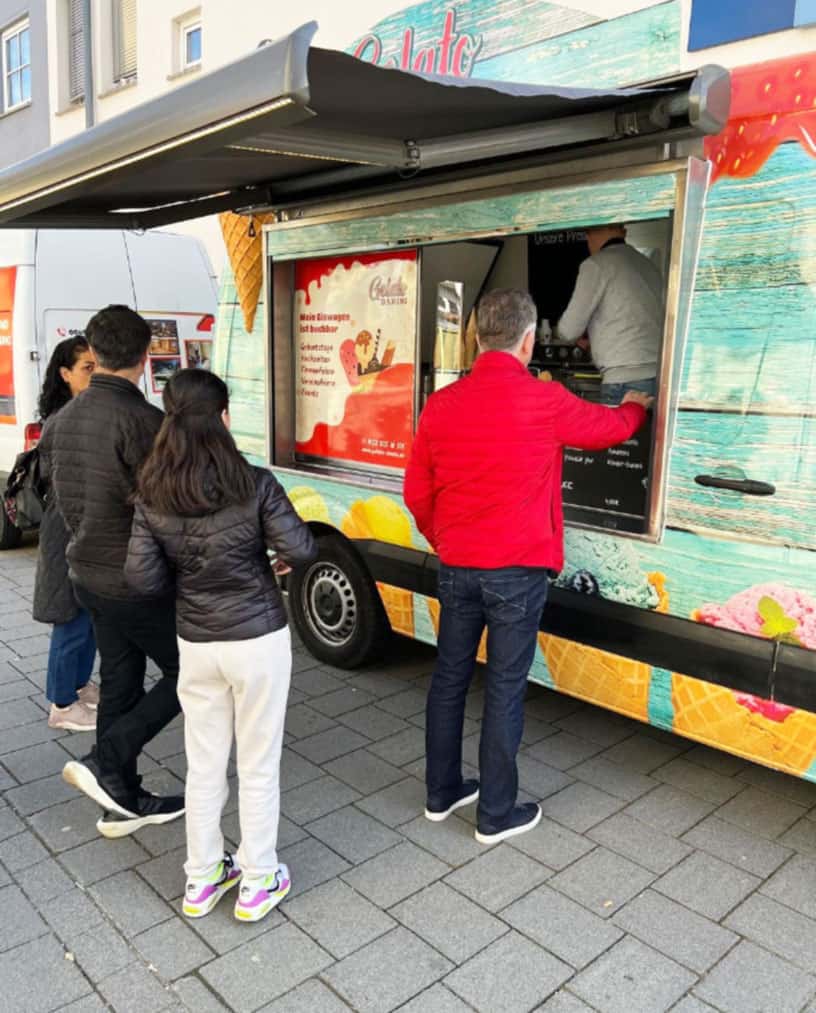 Mann mit einer roten Jacke bekommt ein Eis vom EIswagen